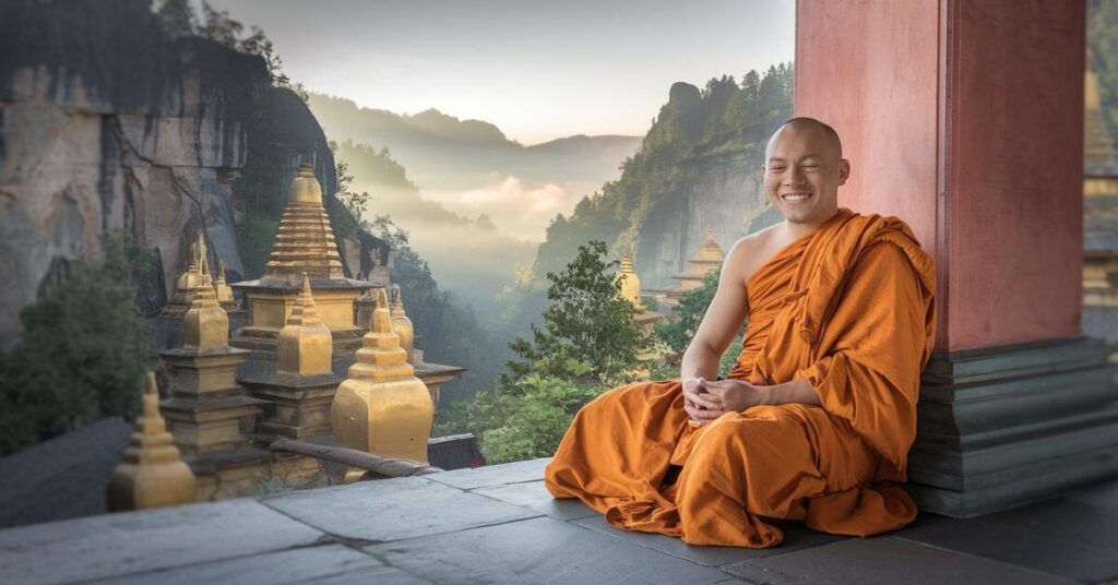 A serene monk sits peacefully on a ledge, gazing out over a breathtaking valley below.